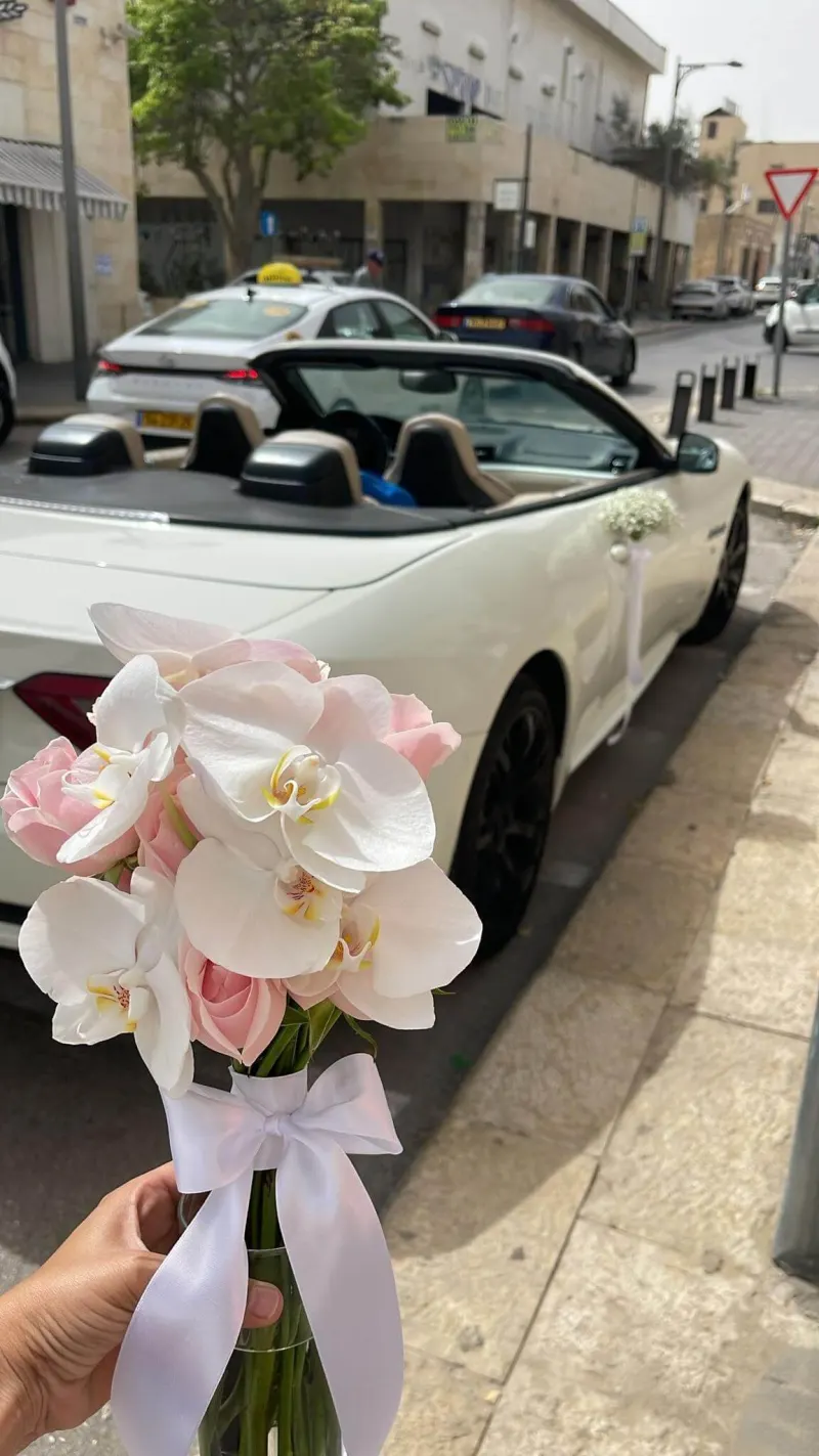 זר סחלבים ורודים ולבנים ליד רכב חתונה